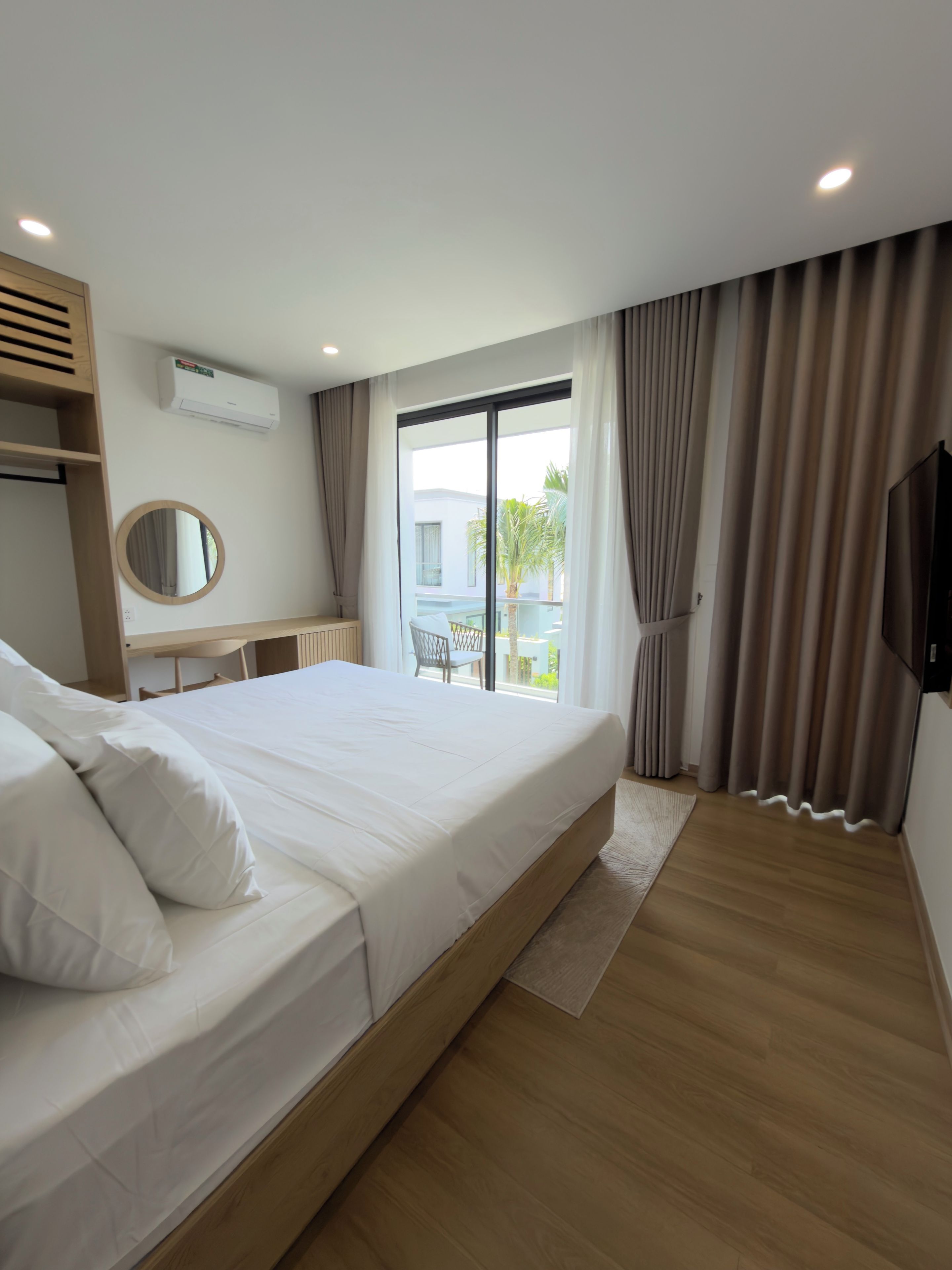 A modern bedroom with a large bed, a desk, a round mirror, and a TV.