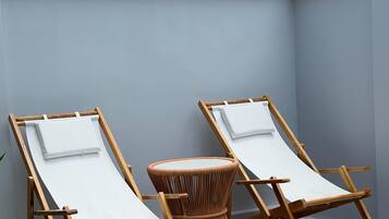 Two wooden lounge chairs with white cushions, a woven round table, and a grey tiled patio area.