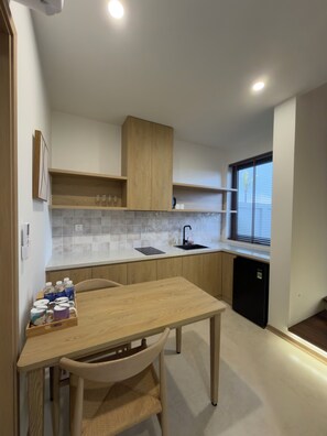 A compact kitchen with a wooden table, a sink, and a window with blinds. - Lagom Residence Phu Quoc (Phu Quoc)