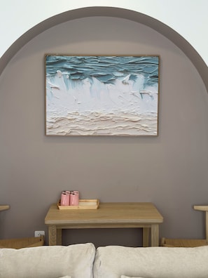 A room with a painting of a beach scene, a wooden table with pink items, and a cushioned bench. - Lagom Residence Phu Quoc (Phu Quoc)