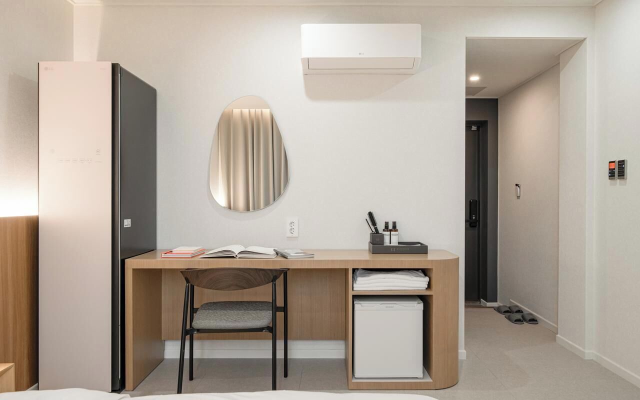 A modern hotel room with a wooden desk, a chair, a small white cabinet, and a wall-mounted air conditioner.