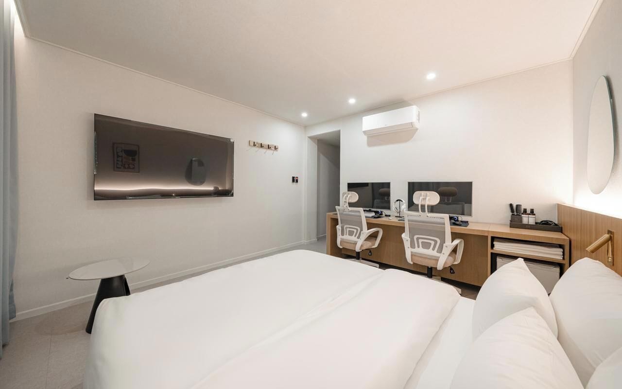 A hotel room with a large bed, a desk with a chair, a mirror, and a TV.