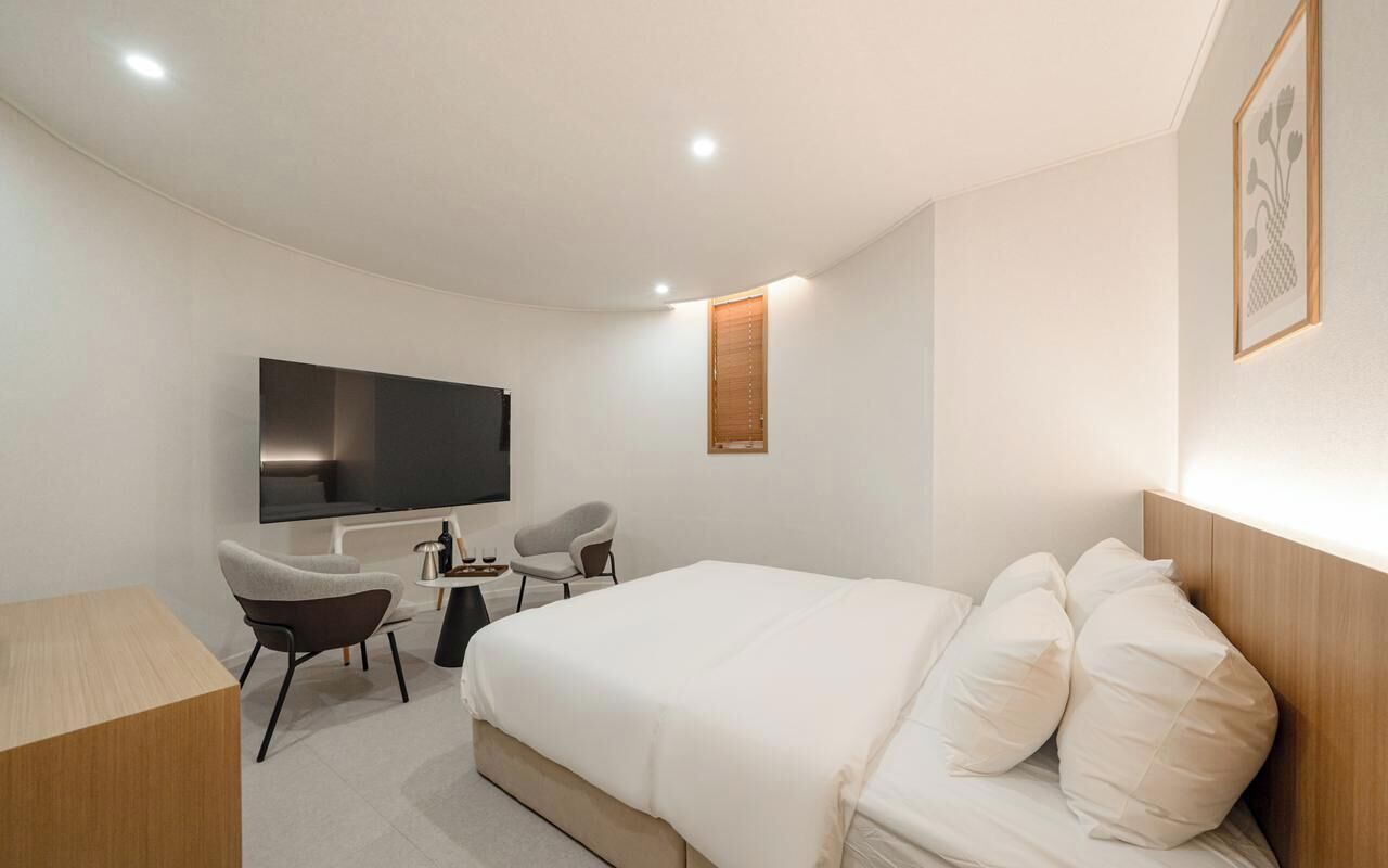 Ein modernes Hotelzimmer mit einem großen Bett, zwei Sesseln, einem Flachbildfernseher und einem Holzkopfende.