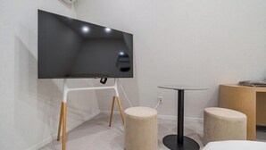 Una camera moderna con una TV a schermo piatto montata su un supporto bianco, un piccolo tavolino rotondo e due pouf.