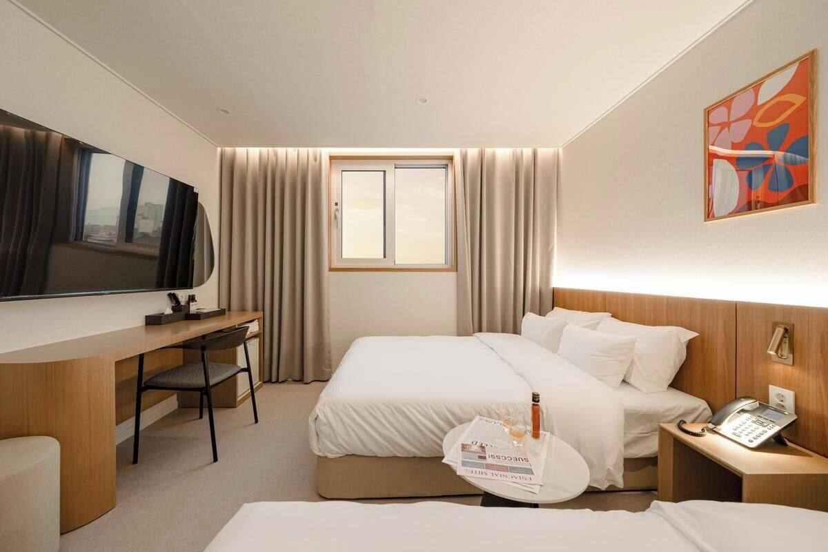 Ein Hotelzimmer mit Bett, Schreibtisch, Stuhl, Fernseher, Fenster und Nachttisch mit Telefon.