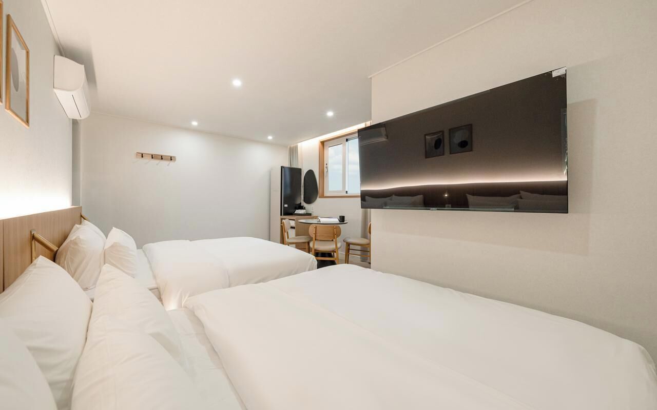 A hotel room with two beds, a desk, a chair, a flat-screen TV, and a large mirror.