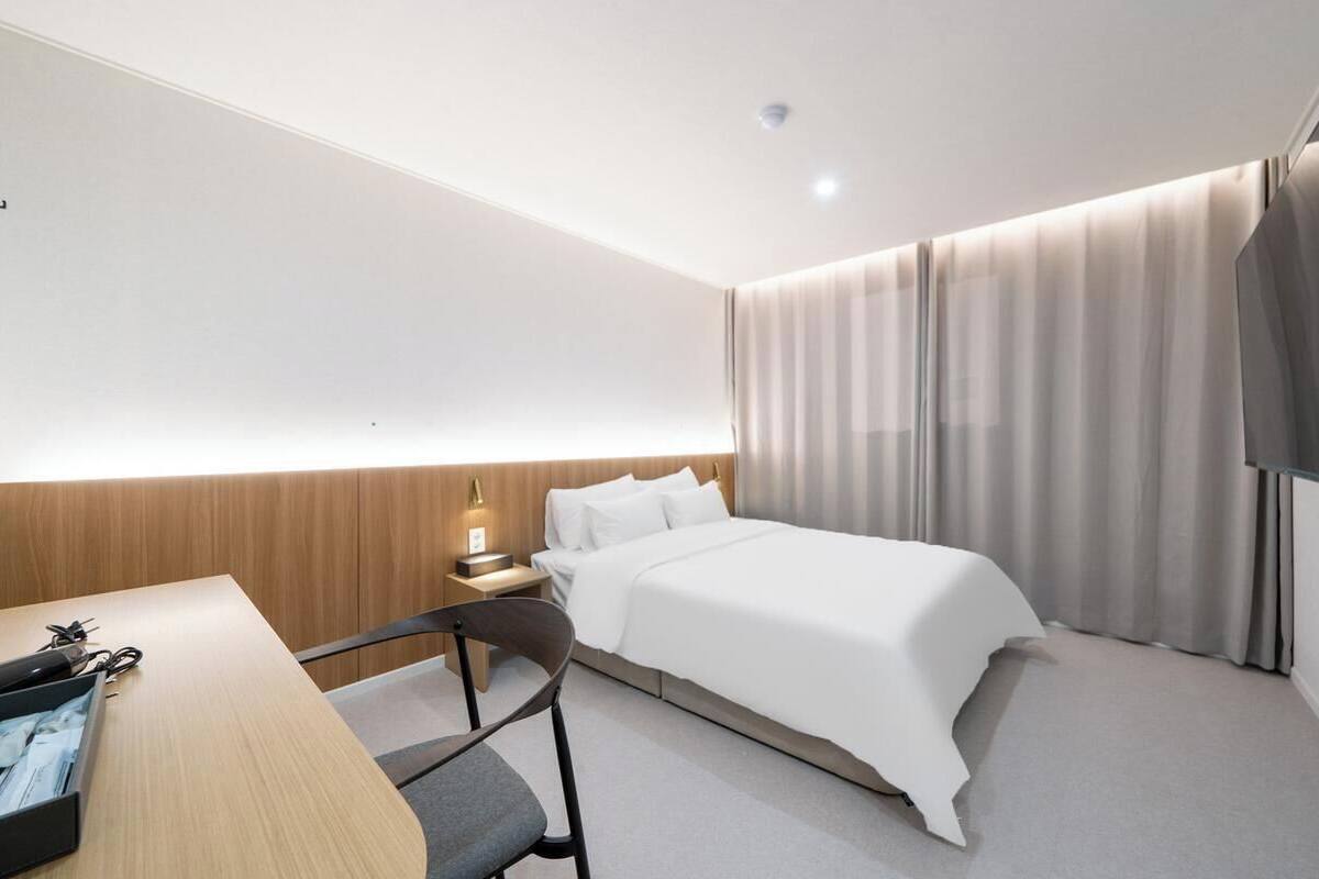Ein modernes Hotelzimmer mit Bett, Schreibtisch, Stuhl, Flachbildfernseher und einem Fenster mit Vorhängen.