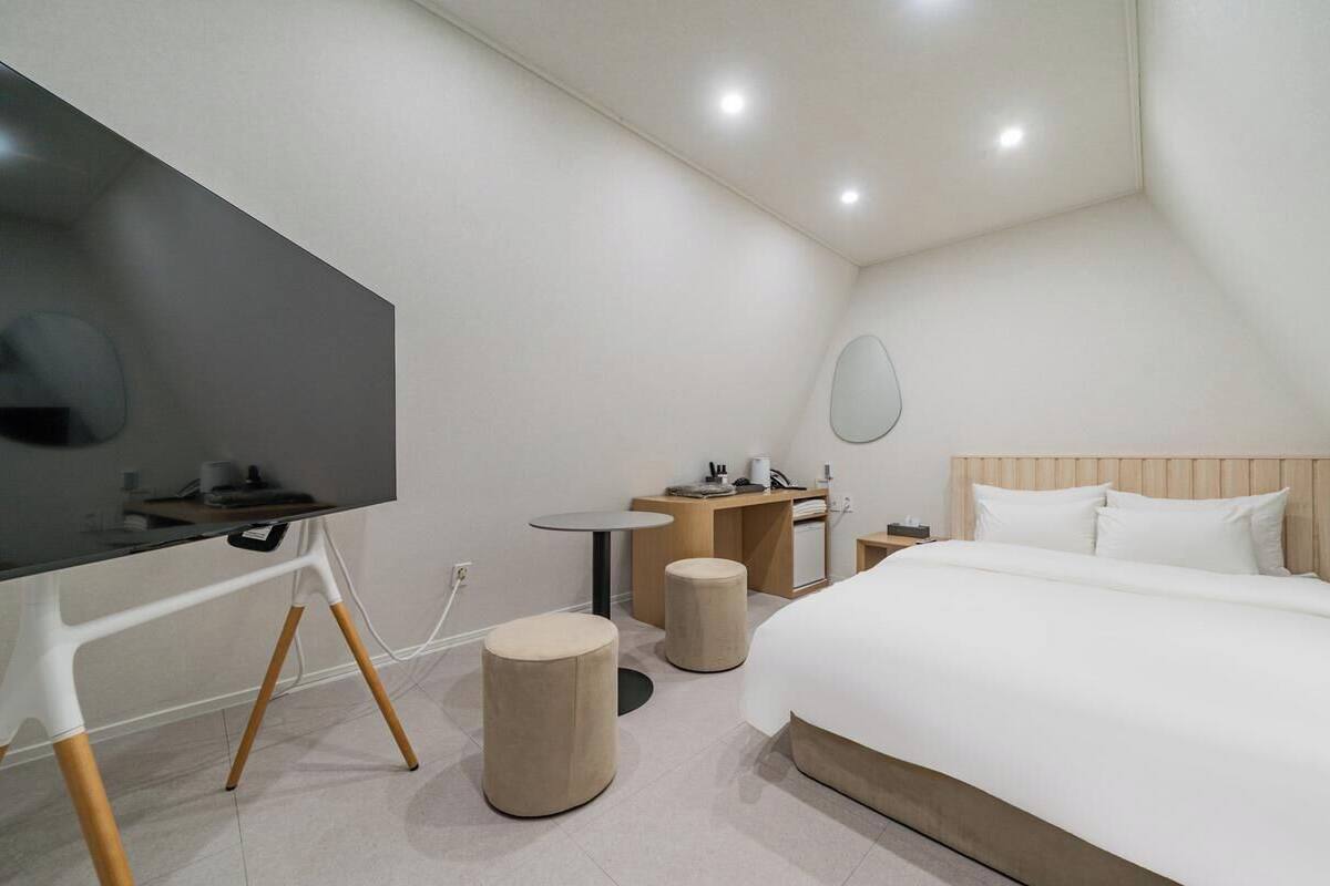 Ein modernes Hotelzimmer mit Bett, Fernseher, Schreibtisch und einem kleinen runden Tisch.