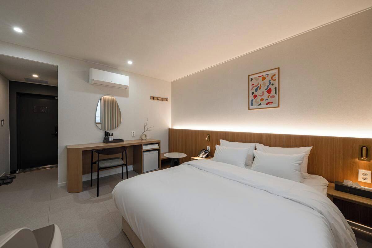 Ein Hotelzimmer mit Bett, Schreibtisch, Stuhl, Nachttisch und einem an der Wand befestigten Telefon.