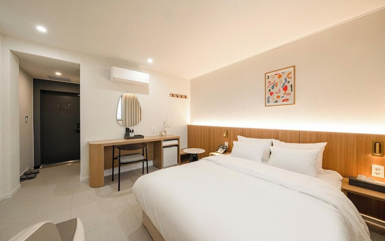 A hotel room with a bed, desk, chair, bedside table, and a small table.