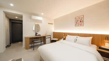 A hotel room with a bed, desk, chair, bedside table, and a small table.