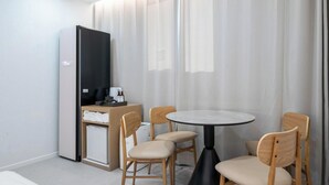 Una camera d'albergo con un letto, una piccola scrivania con un computer, un tavolo rotondo con sedie e un'ampia finestra con tende.