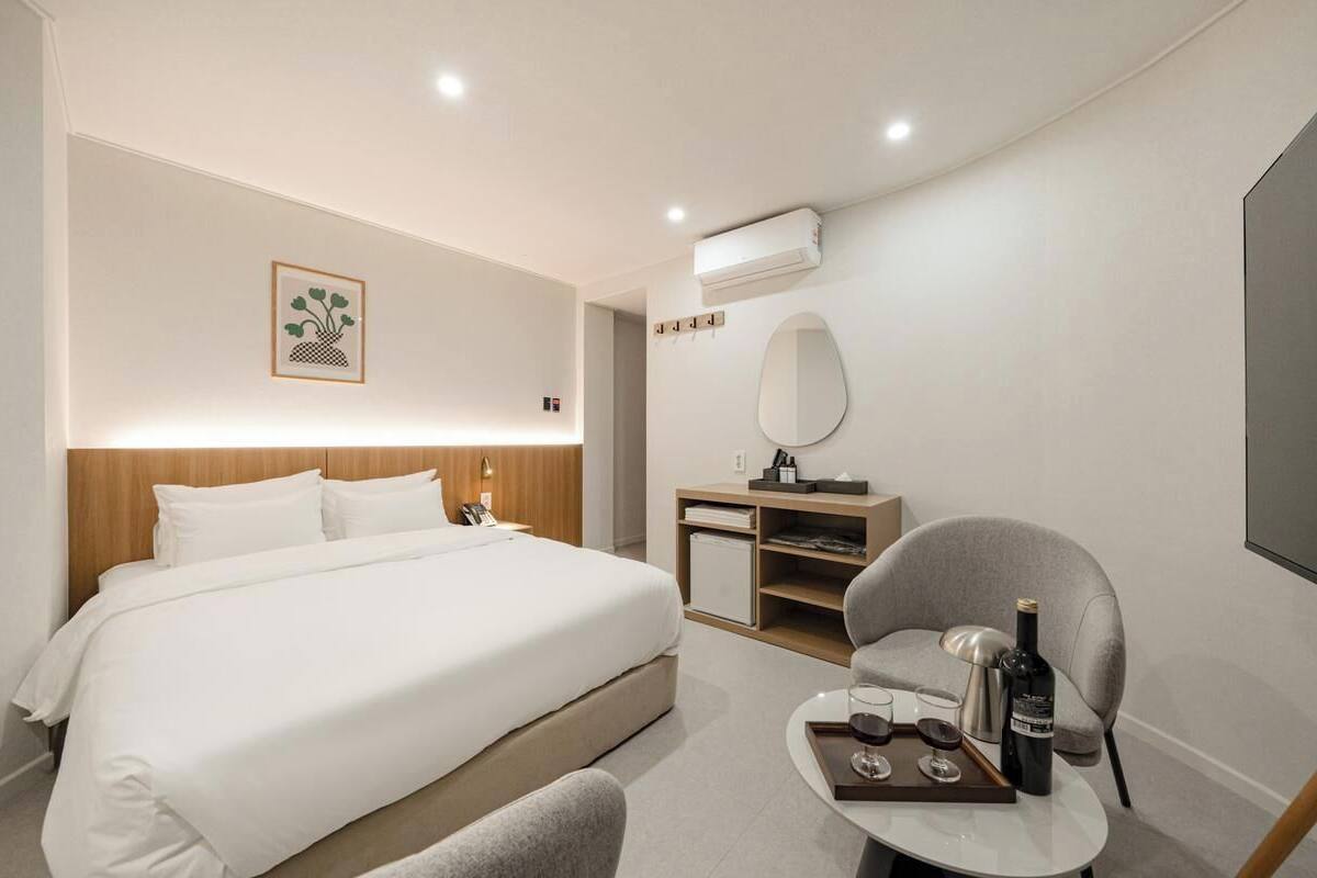 Ein Hotelzimmer mit Bett, Stuhl, kleinem Tisch mit Flasche und Gläsern, Spiegel und einem Bild an der Wand.