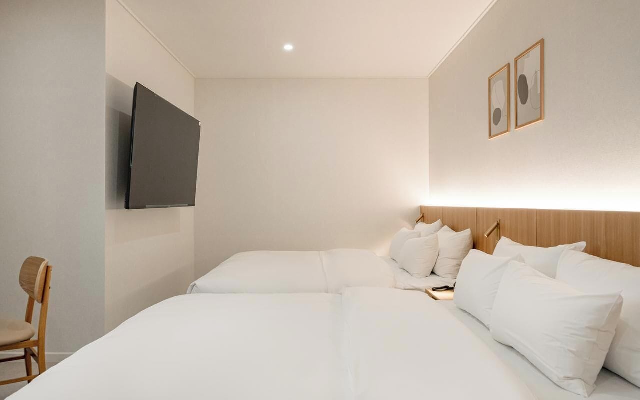 A hotel room with a large bed, a flat-screen TV mounted on the wall, and a wooden headboard.
