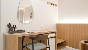 Una camera moderna con una scrivania in legno, una sedia, uno specchio e un piccolo ripiano con articoli da toilette.