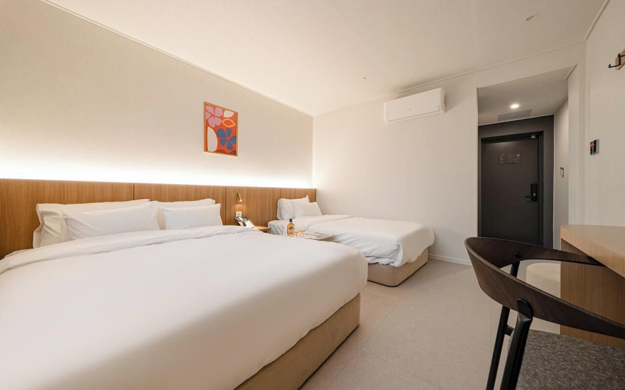 Habitación de hotel con dos camas, un escritorio, una silla y una puerta.