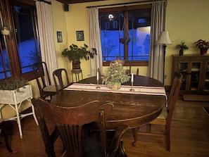 A dining room with a wooden table, chairs, a potted plant, and a window with curtains.