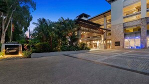 A hotel entrance with a sign for Pullman Palm Cove & Palm Resort, a covered walkway, and a landscaped area with trees. - Temple 3 Bedroom 214 (Palm Cove)
