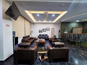 Un hall d’hôtel avec des canapés en cuir, un comptoir de réception, un distributeur d’eau et un espace d’accueil agrémenté d’un mur en pierre.