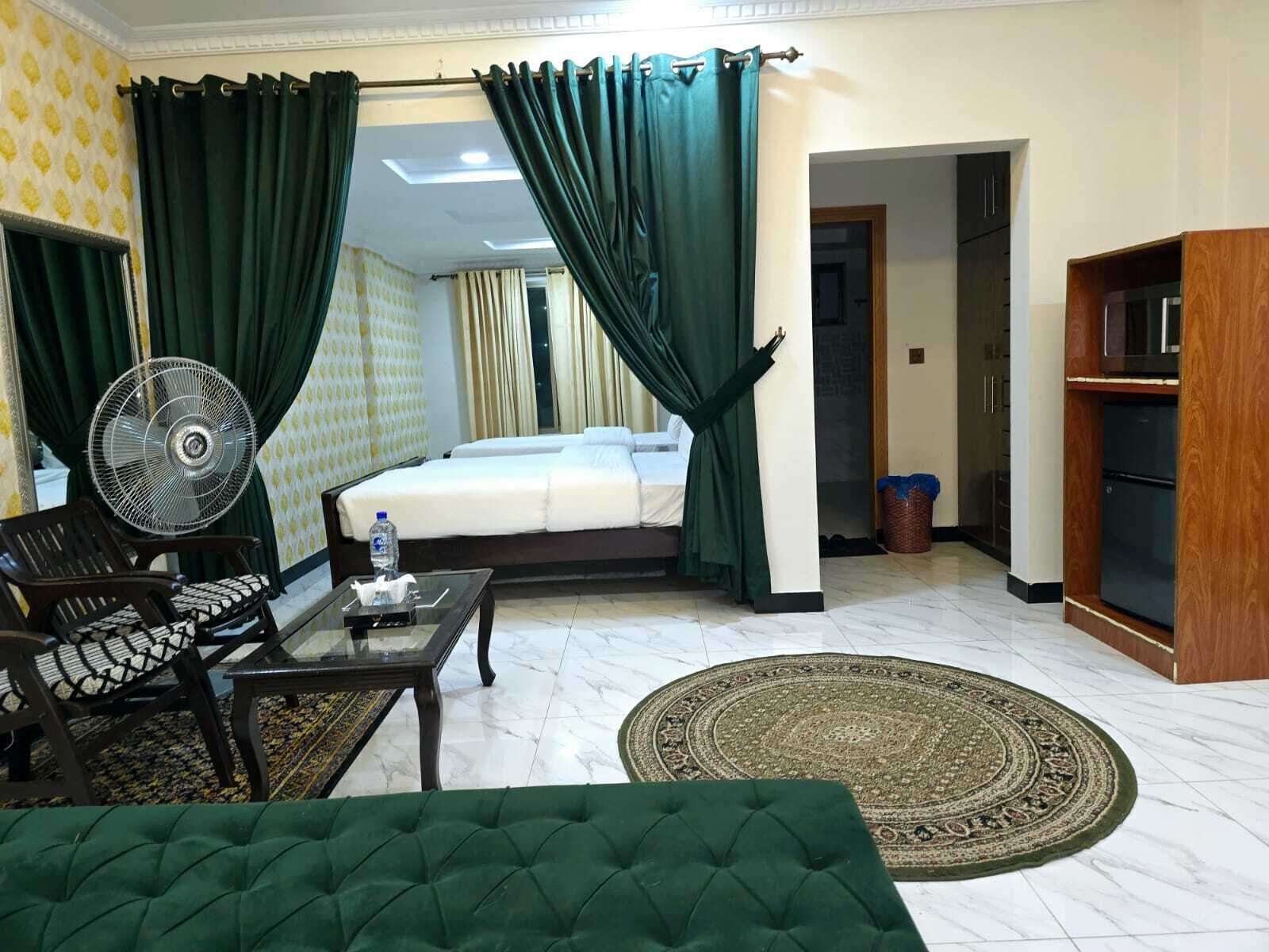 Habitació d'hotel amb un llit, un ventilador, un sofà, una taula de cafè i una catifa.
