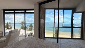 Ein modernes Schlafzimmer mit großen Fenstern, einem Marmorkopfschild und Blick auf Strand und Meer.