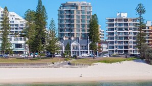 Ein Hotel an der Küste mit mehreren Stockwerken, einem Strand im Vordergrund und umgebender Bepflanzung.