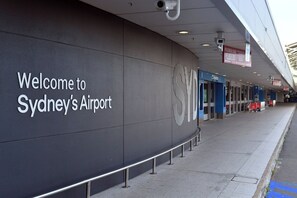 The exterior of Sydney's Airport with a 'Welcome to Sydney's Airport' sign, a security camera, and a departure sign. - KozyGuru | Brighton-Le-Sands | Luxury Bay View Apt (Brighton-Le-Sands)