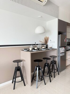 A modern kitchen with a central island, bar stools, a hanging light fixture, and a refrigerator. - Luxury 4Pax Studio | Bathtub | Foosball | Parking (Kuala Lumpur)