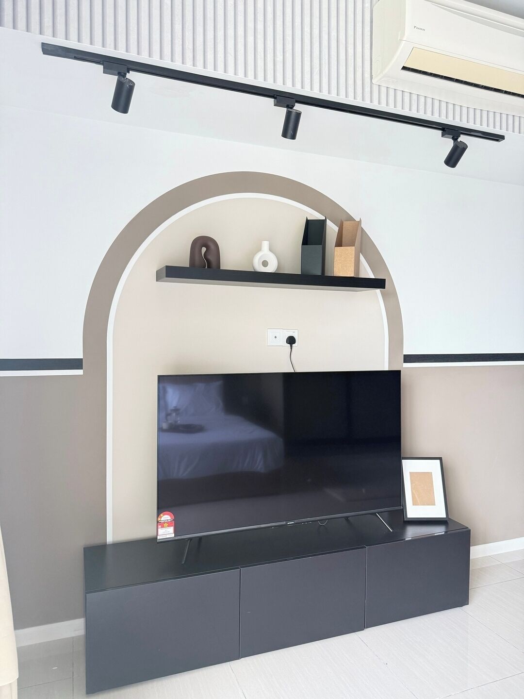 Un salon moderne avec un téléviseur à écran plat fixé sur un meuble noir, un mur blanc doté d’une étagère encastrée et un appareil de climatisation fixé au plafond.