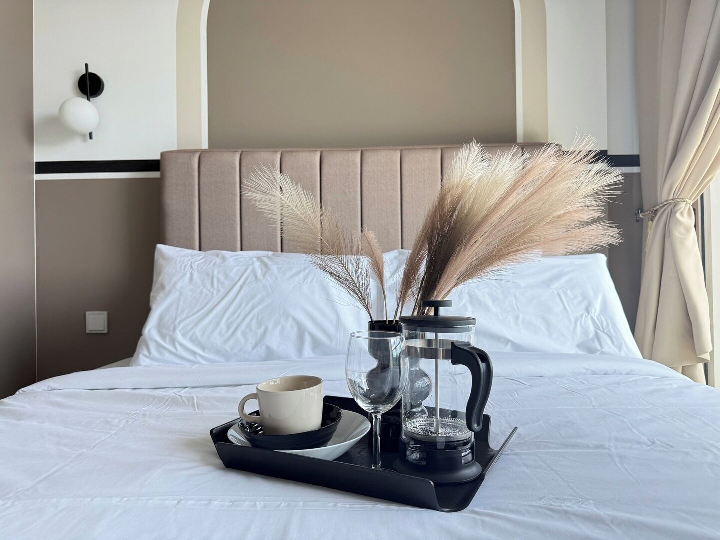 Un lit bien fait, sur lequel se trouve un plateau avec une tasse, un verre et une cafetière, le tout agrémenté de quelques brins de graminée des pampas.