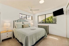 A bedroom with a bed, nightstands, a ceiling fan, a TV, and a window with a view. - 4/16 Leeding Terrace, Caloundra QLD 4551 (Sunshine Coast)
