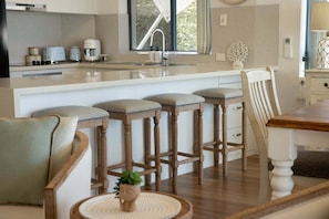A kitchen with a central island, bar stools, a dining table, and a chair. - 4/16 Leeding Terrace, Caloundra QLD 4551 (Sunshine Coast)