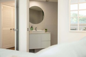 A bathroom with a round mirror, a sink, and a window. - 4/16 Leeding Terrace, Caloundra QLD 4551 (Sunshine Coast)