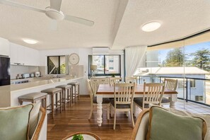 A modern kitchen with a dining area, large windows, and a ceiling fan. - 4/16 Leeding Terrace, Caloundra QLD 4551 (Sunshine Coast)