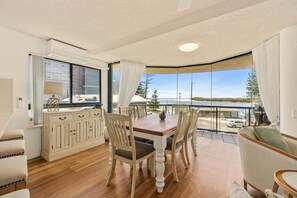 A dining area with a wooden table and chairs, a cabinet with drawers, and a view of the outdoors through large windows. - 4/16 Leeding Terrace, Caloundra QLD 4551 (Sunshine Coast)