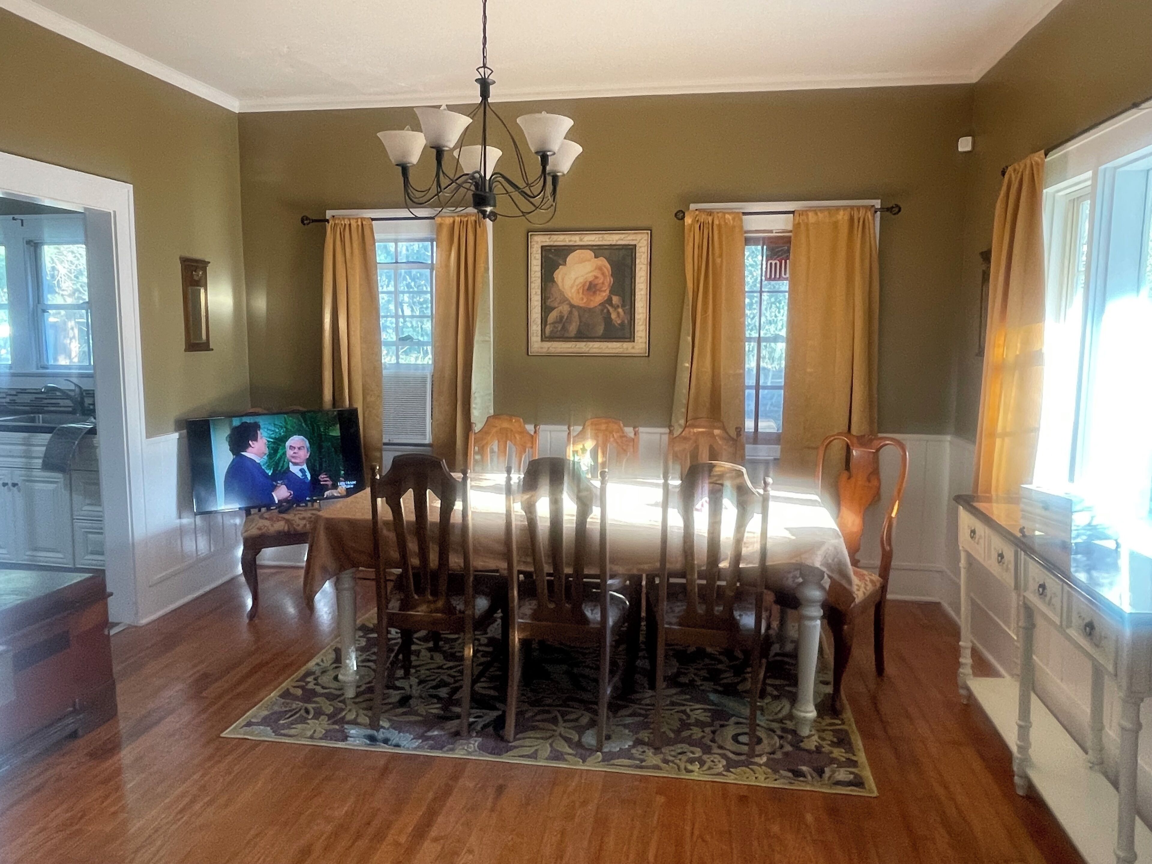 A dining room with a wooden table, chairs, a chandelier, and a television.