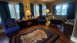 Un salon avec un piano, un fauteuil bleu, un tapis et une lampe.