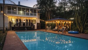 Une maison à deux étages avec une piscine, un espace salon extérieur et des guirlandes lumineuses.