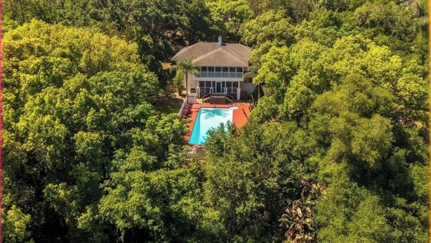 Une maison entourée d’une forêt dense, avec une piscine à l’avant.