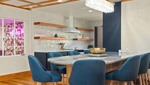 Eine moderne Küche mit einer zentralen Kochinsel, blauen Barhocker und einem Kronleuchter.