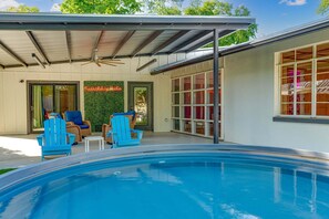 A pool area with blue chairs, a ceiling fan, and a green wall. - Tipsy Peach | Heated Cowboy Pool | Walk to Main (Fredericksburg)