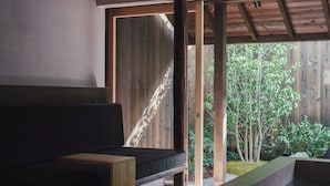 A room with a wooden bench, a small table, and a view of a garden with trees and plants. - MUDANI DARUMACHO (Kyoto)