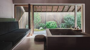 A modern interior with a wooden ceiling, a black sofa, a stone basin, and a view of a garden. - MUDANI DARUMACHO (Kyoto)