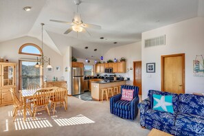 A spacious living area with a dining table, chairs, a blue sofa, and a kitchen in the background. - Always Dreaming - Corolla, Ocean Sands, 150 Yds to Beach, Oceanside, Pool, Hot Tub, Pets OK (Corolla)