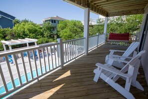 A wooden deck with white railings, a pool, and a red towel on a chair. - Always Dreaming - Corolla, Ocean Sands, 150 Yds to Beach, Oceanside, Pool, Hot Tub, Pets OK (Corolla)