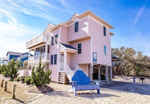 A pink two-story building with a balcony, a staircase, and a signboard. - Always Dreaming - Corolla, Ocean Sands, 150 Yds to Beach, Oceanside, Pool, Hot Tub, Pets OK (Corolla)