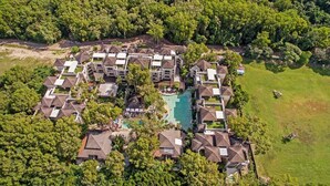 An aerial view of a resort with multiple buildings, a central swimming pool, and surrounding greenery.