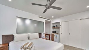 A hotel room with a bed, a ceiling fan, a desk, a microwave, and a wardrobe.