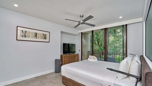 A bedroom with a bed, a ceiling fan, a TV, a balcony, and a framed picture on the wall.