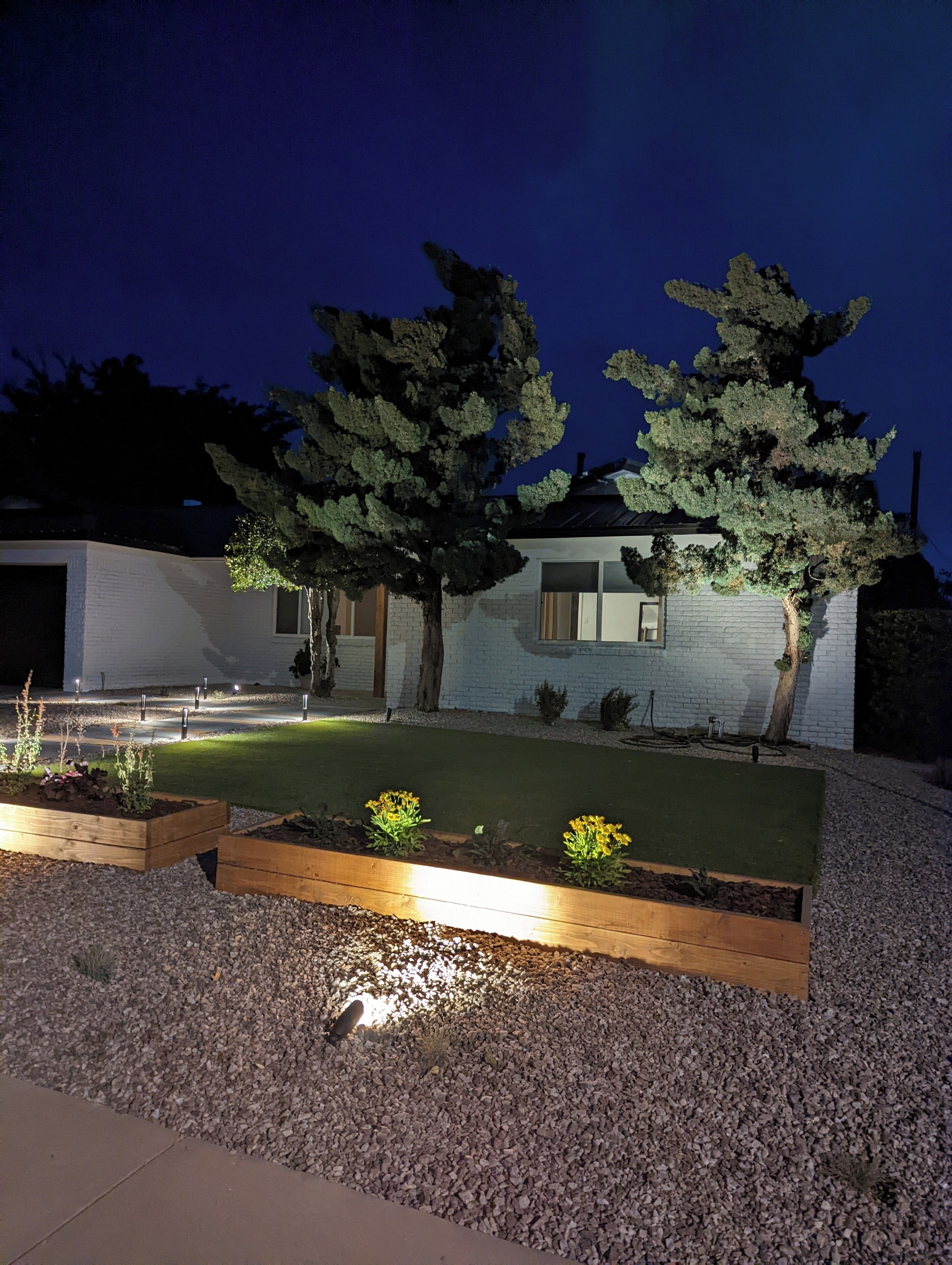 Une maison moderne dotée d’un jardin bien éclairé, d’une allée pavée et d’une façade blanche.